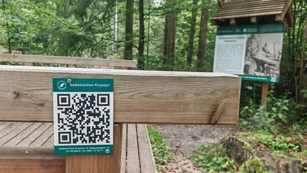 Tabliczka z kodem QR przy tablicy edukacyjnej.
